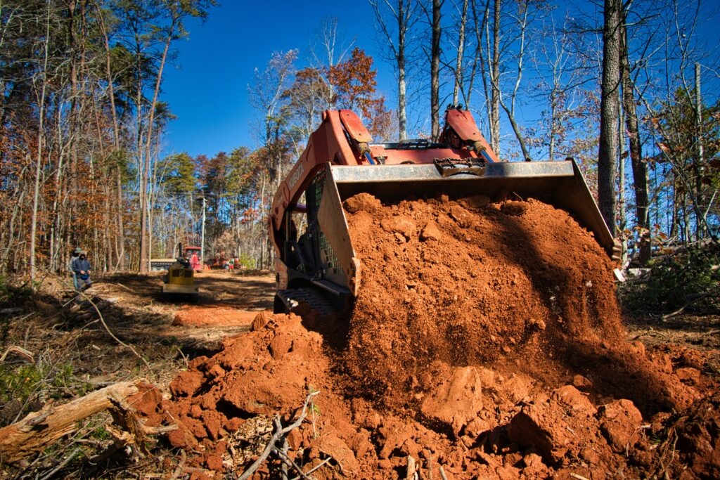 A red dumper truck is moving a large amount of earth to the foreground of the image.